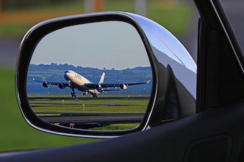 Reflet d'un avion à travers le miroir d'un rétro-viseur d'une voiture de location